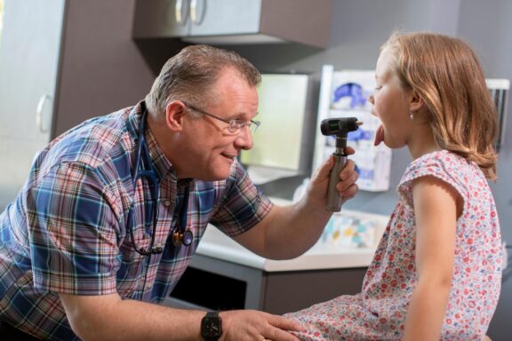 A doctor uses an otoscope to examine a young patient’s throat, creating a friendly and engaging interaction to ensure the child feels comfortable during the check-up.