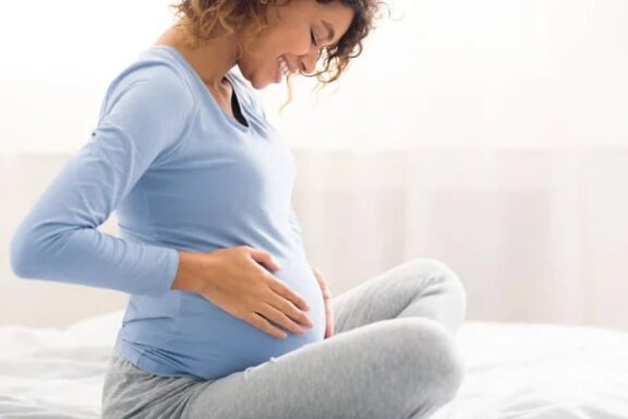 Pregnant woman sitting comfortably, smiling and holding her belly, focusing on prenatal health and wellness.